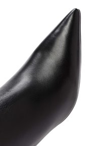 Zapato de tacón alto de cuero negro con punta afilada, superficie lisa y diseño elegante, que presenta una apariencia minimalista y pulida.