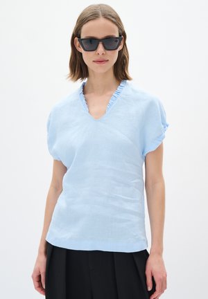 Haut bleu clair à manches courtes avec un col en V et un col à volants. Fabriqué dans un matériau léger, coupe ample, associé à un pantalon noir.