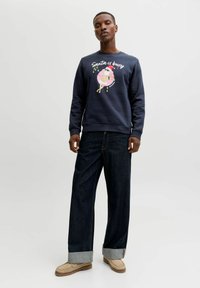 Námořnický svetr s grafikou "Santa je zaneprázdn�ěný" a barevnou ilustrací, v kombinaci s volnými tmavými džínami a hnědými botami. Jednoduchý design.