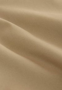 Gros plan sur un tissu beige lisse et finement tissé avec une texture nervurée diagonale délicate et des plis doux créant des ombres légères.