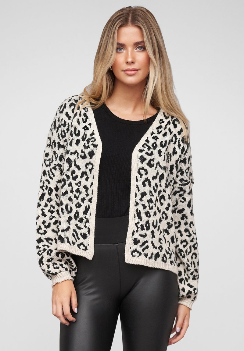 Strikket cardigan med leopardmønster i svart og krem. Har en cropped lengde og ribbede mansjetter, lagt over en svart teksturert topp.