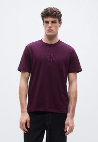 Burgundy cotton t-shirt with a crew neckline and short sleeves, featuring a small embroidered CK logo on the chest.