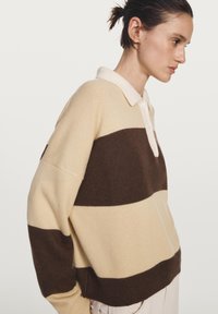 Krémovo-hnědý proužkovaný pletený svetr s bílým límcem a knoflíkovou légu. Oversized střih s žebrovanými manžetami a lemem. Měkká textura.