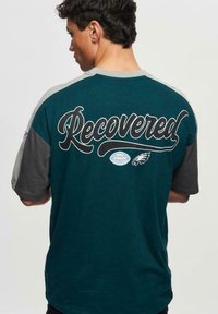 Vihreä ja harmaa lyhythihainen t-paita, jossa on "Recovered"-teksti selässä ja Eagles-logo; puuvillaa, rento istuvuus, pyöreä kaula-aukko.