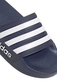 Granatowe klapki z trzema białymi paskami i wytłoczonym logo. Wykonane z teksturowanego materiału syntetycznego z płaską gumową podeszwą.