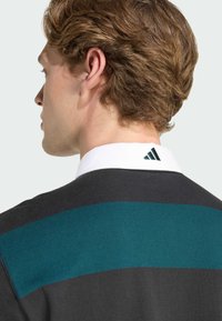 Polo pour homme en gris foncé avec des rayures horizontales teal. Doté d'un col blanc avec un logo brodé à l'arrière. Texture de tissu douce.