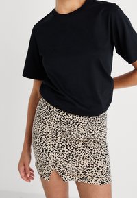 Černé bavlněné tričko v kombinaci s upnutou béžovou mini sukni s černým leopardím potiskem a mírným rozparkem na dolním lemu.