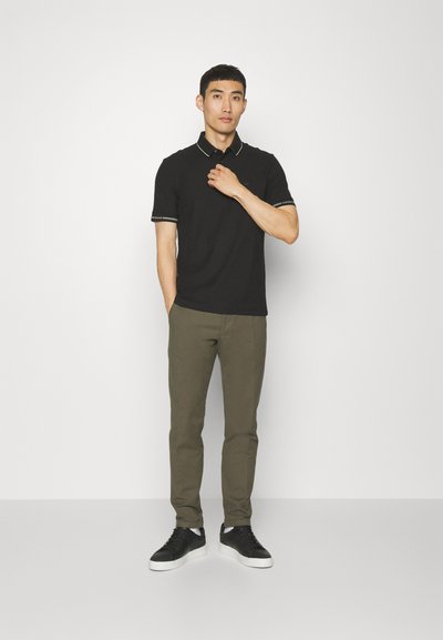 Black polo shirt with contrasting collar and sleeve accents, paired with olive green slim-fit pants and black sneakers. Minimalistic design.