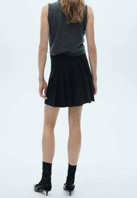 Jupe plissée noire associée à un haut gris sans manches. La tenue comprend des épaules ajustées et des chaussures à talons hauts sombres et brillantes.