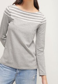 Haut à manches longues rayé gris avec un col rond. La partie supérieure présente des rayures blanches plus larges, tandis que la partie inférieure a des rayures plus étroites.