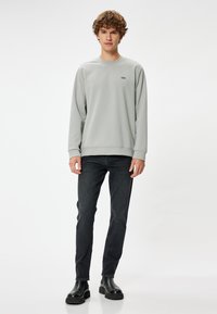 Grå långärmad sweatshirt med rund halsringning, med en liten svart logotyp. Kombinerad med mörka jeans och svarta ankelskor. Slät textur.