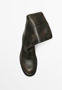 Ciemnozielony skórzany botek na kostkę o luźnym kroju, zaokrąglonym nosku i teksturowanej podeszwie. Posiada miękkie wykończenie z minimalnymi akcentami przeszyć.