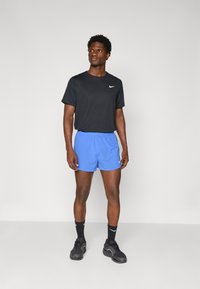 Schwarzes T-Shirt mit kurzen Ärmeln und weißem Nike-Logo, blaue Shorts, schwarze Sportschuhe und schwarze Socken. Schlichtes Design, leichtes Material.