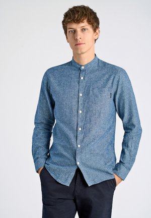 Camisa de chambray azul de manga larga con cuello de botón, bolsillo frontal y botones blancos, con una tela texturizada.