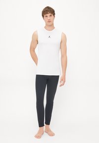 White sleeveless shirt with a black Jordan logo, paired with black fitted leggings. The fabric appears smooth and stretchy.