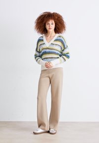 Striped knitted sweater in light greens, blues, and white, featuring a V-neck and textured material. Paired with beige wide-leg pants and silver shoes.
