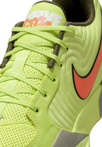 Sneaker verde neon con mesh strutturato, pannello laterale ondulato, swoosh Nike arancione, occhielli rinforzati e lacci verde brillante.