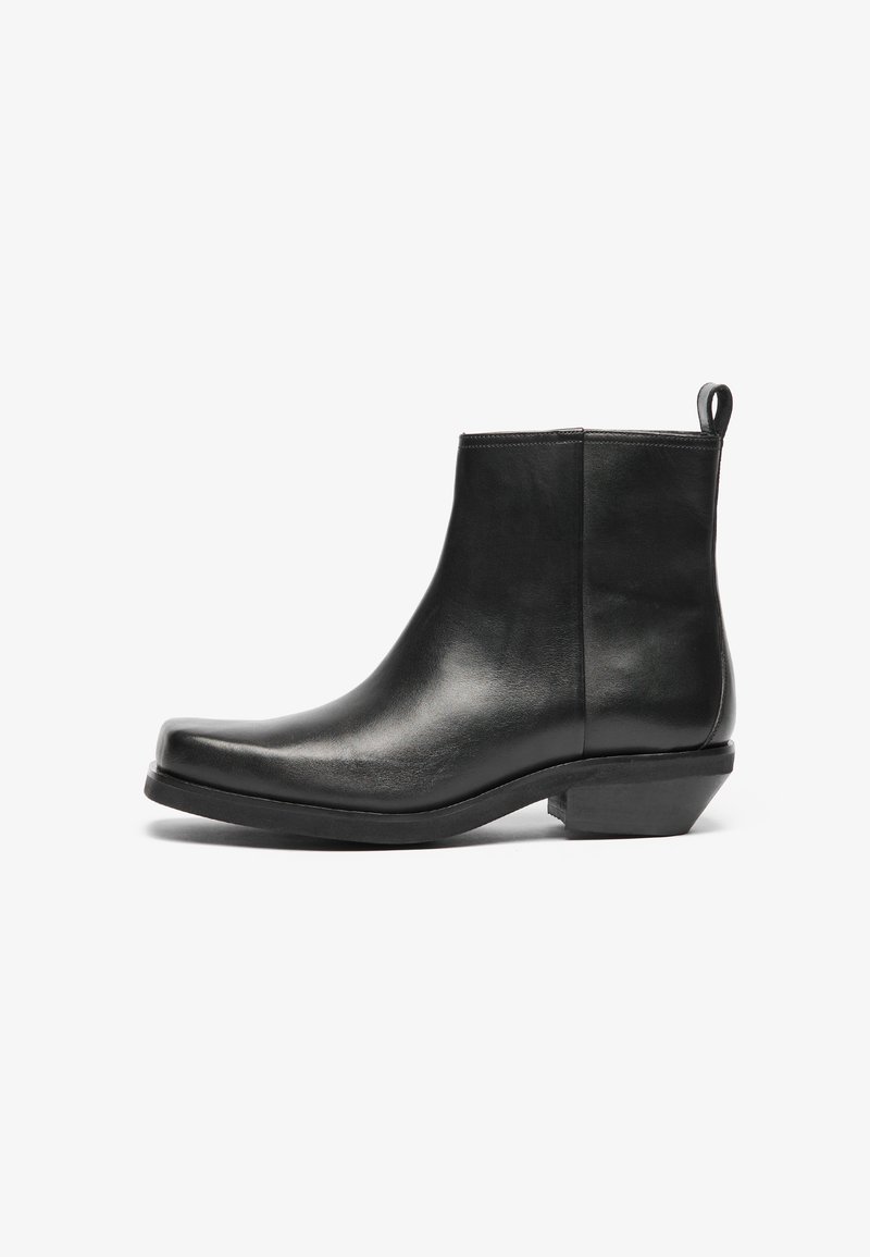 Botas negras de cuero hasta el tobillo con punta afilada y tacón bajo. Diseño elegante con una textura suave y una cinta de tirón para facilitar su uso.