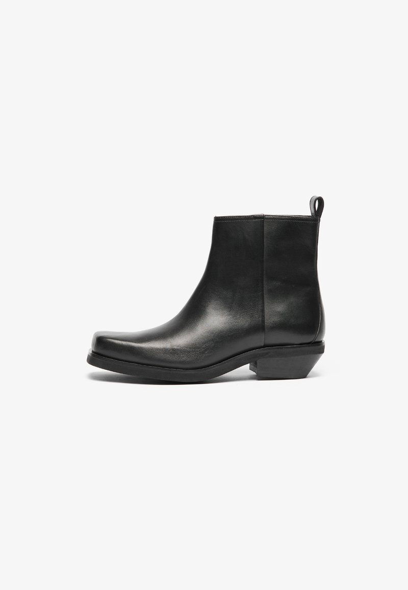 Bottines en cuir noir avec un bout effilé et un petit talon bloc. Design épuré avec une texture lisse et une languette pour un enfilage facile.