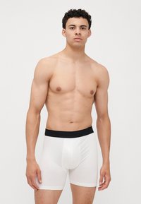 Weiße Baumwollboxershorts mit schwarzem Elastikbund. Glatte Textur, enganliegendes Design und Länge bis zur Mitte des Oberschenkels. Keine Muster oder Verzierungen.