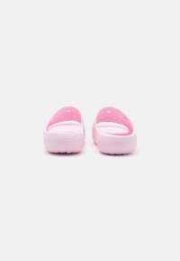 Rozā Crocs ar gludu tekstūru, atvērtu aizmuguri un ventilācijas caurumiem. Tam ir balta zole ar iepresētu logotipu aizmugurē.