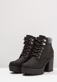 Black ankle boots featuring a chunky platform sole, faux suede material, silver hardware, and black laces with silver accents.