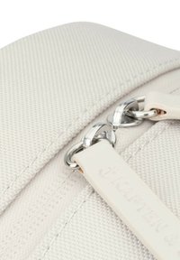 Biały płócienny worek z teksturowaną powierzchnią, metalowy zamek błyskawiczny z srebrnymi akcesoriami oraz materiałowa metka z wytłoczonym logo marki.