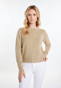 Beige Strickpullover mit Rundhalsausschnitt, gerippten Bündchen und Saum. Weicher Stoff, lässiger Schnitt, kombiniert mit weißen, eng geschnittenen Hosen.