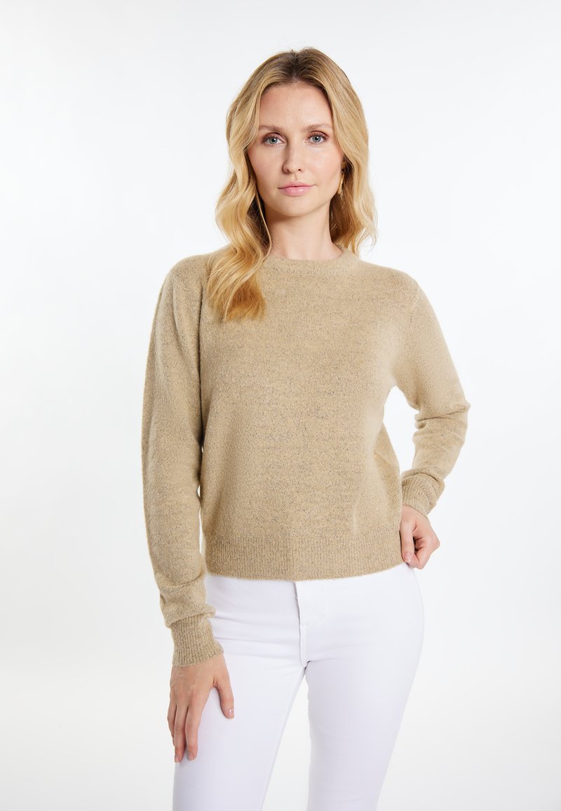 Beige Strickpullover mit Rundhalsausschnitt, gerippten Bündchen und Saum. Weicher Stoff, lässiger Schnitt, kombiniert mit weißen, eng geschnittenen Hosen.