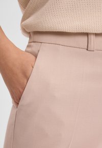 Jasnoróżowe spodnie wykonane z gładkiego materiału, z boczną kieszenią i dopasowanym krojem. W pasie znajduje się detal w postaci szlufki na pasek.