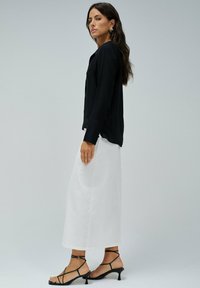 Top de manga larga negra, falda blanca fluida y sandalias negras con tiras. Texturas de tela suaves, top ajustado y falda ancha hasta los tobillos.