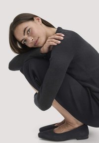 Ein schwarzer Strickpullover und passende Hosen bilden ein elegantes, monochromes Outfit. Viereckige schwarze Ballerinas vervollständigen den Look. Sanfte Textur durchgehend.
