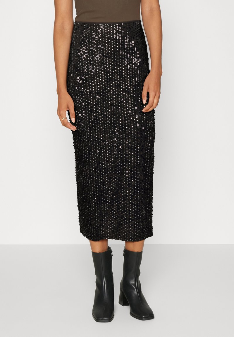 Černá midi sukně s flitry a úzkým střihem, s texturovaným povrchem a podšívkou. Kombinována s černými kotníkovými botami na podpatku.