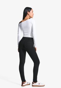Svarta smala jeans, vit långärmad tröja och vita sneakers med bruna detaljer. Slitstark tyg, kroppsnära passform och minimalistiska detaljer.