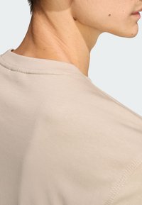 Béžové bavlnené tričko, detail zadného výstrihu, s hladkou textúrou a viditeľnými švami pozdĺž švu.