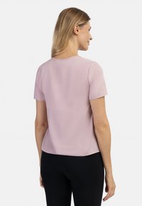 Krótki rękaw, bluzka w miękkim różowym materiale, z okrągłym dekoltem i luźnym krojem. Gładka tekstura z lekkim połyskiem, stylizowana z minimalnymi detalami.