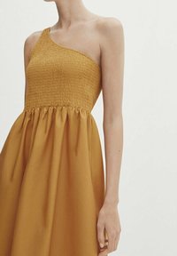 Robe asymétrique jaune moutarde, dotée d'un corsage smocké et d'une jupe fluide. Texture lisse avec un haut ajusté et un bas ample.
