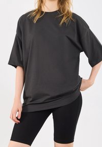 T-shirt nera oversize con maniche corte, realizzata in tessuto morbido, abbinata a pantaloni biker neri a coste. Design semplice, vestibilità rilassata.
