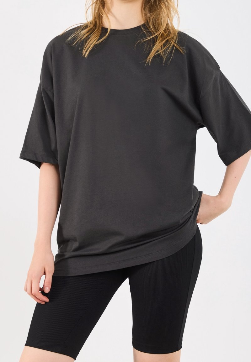T-shirt nera oversize con maniche corte, realizzata in tessuto morbido, abbinata a pantaloni biker neri a coste. Design semplice, vestibilità rilassata.