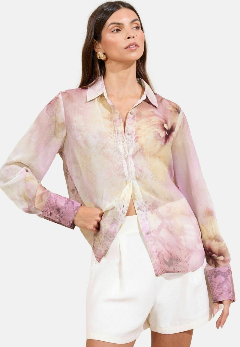 Transparante button-up blouse in pastelroze met bloemenpatronen; lange mouwen met bedrukt manchet; gecombineerd met witte op maat gemaakte korte broeken.
