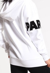 Felpa bianca con cappuccio e testo "PAR" nero sulla manica sinistra. Presenta una vestibilità comoda e polsini e orlo a costine. Tessuto morbido.