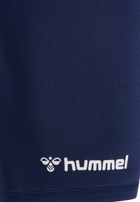Marinblå träningsshorts i ett slätt, elastiskt material. Har en vit "hummel"-logotyp och ett bi-emblem nära nederkanten.