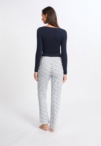 Marinblå långärmad tröja tillsammans med vita byxor med blommönster. Tyget är mjukt och byxorna har en avslappnad passform med resårmidja.
