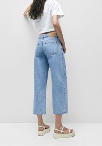 Lichtblauwe denim wide-leg jeans met een cropped snit, voorzien van achterzakken en een tan leren patch op de taille. Gepaard met witte platform sandalen.