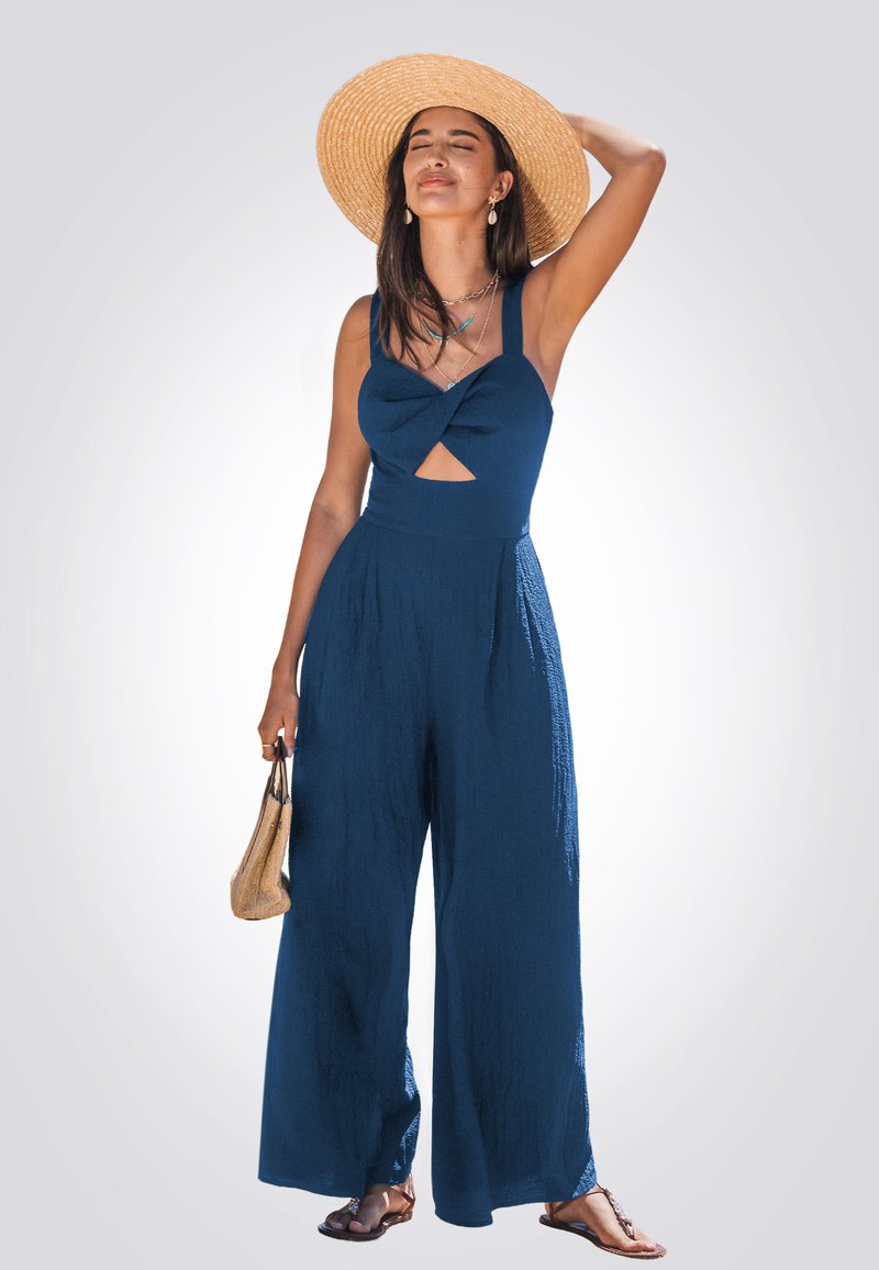 Jumpsuit strutturato di colore blu navy con pantaloni a gamba larga; presenta un corpetto annodato, dettagli con cut-out e spalline sottili. Abbinato a un cappello di paglia.