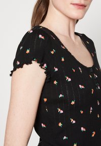 Černý žebrovaný top s krátkými volánovými rukávy, s květinovým vzorem v růžové, oranžové a zelené barvě, a s kulatým výstřihem a knoflíky.