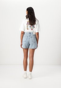Vitt t-shirt med en illustrerad design som föreställer en byggnad och blommor på ryggen, ihop med ljusblå denimshorts.