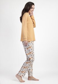 Top de manga larga mostaza combinado con pantalones de pijama estampados que presentan ilustraciones de animales en naranja, gris y negro sobre un fondo claro.