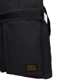 Gilet matelassé noir avec une texture lisse, doté d'une poche horizontale et d'une étiquette tissée avec la marque et les spécifications. Détails de sangle inclus.