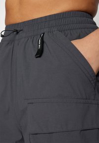 Harmaat cargo-shorts, joissa on joustava vyötärö, nauha, sivutasku ja kangasmerkki esillä. Valmistettu kevyestä ja kestävästä materiaalista.